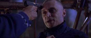 Movie still from “The World Is Not Enough” (1999), directed by Michael Apted – A man with a gun on his head and another man holding a gun pointed at him; Close Up shot, Over the shoulder angle