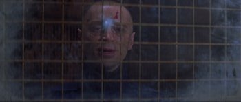 Movie still from “The World Is Not Enough” (1999), directed by Michael Apted – A bald man with a shaved head looking through a cage; Close Up shot, Over the shoulder angle