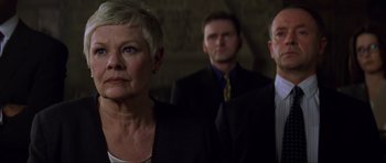 Movie still from “The World Is Not Enough” (1999), directed by Michael Apted – A woman standing next to two men wearing suits; Close Up shot, Low angle