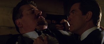 Movie still from “The World Is Not Enough” (1999), directed by Michael Apted – Two men in a dark room with one holding a gun and the other holding a gun; Close Up shot, Over the shoulder angle