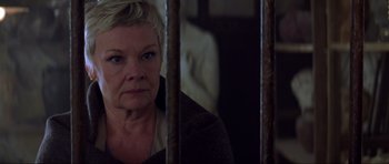 Movie still from “The World Is Not Enough” (1999), directed by Michael Apted – An older woman sitting behind bars in a room; Close Up shot, Low angle