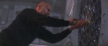 Movie still from “The World Is Not Enough” (1999), directed by Michael Apted – A man in a black shirt is washing a machine; Medium shot, Low angle