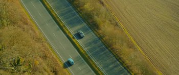 Movie still from “The World's End” (2013), directed by Edgar Wright – Two cars driving down a road near a field; Extreme Wide shot, Overhead angle
