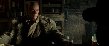 Movie still from “The World's End” (2013), directed by Edgar Wright – A man with a bald head sitting at a table with a glass of beer in front of him; Close Up shot, Low angle
