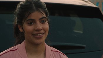 Movie still from “Theater Camp” (2023), directed by Molly Gordon – A woman in a pink shirt smiling for the camera; Close Up shot, Over the shoulder angle