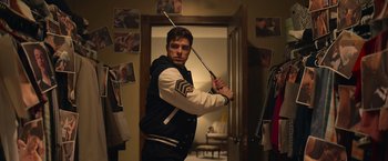 Movie still from “There's Someone Inside Your House” (2021), directed by Patrick Brice – A man holding a stick in a room; Medium shot, Over the shoulder angle