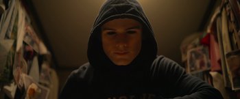 Movie still from “There's Someone Inside Your House” (2021), directed by Patrick Brice – A young man wearing a hooded sweatshirt stares into the camera; Close Up shot, Low angle