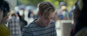 Movie still from “There's Someone Inside Your House” (2021), directed by Patrick Brice – A young man smoking a cigarette while wearing a striped shirt; Close Up shot, Low angle
