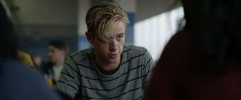 Movie still from “There's Someone Inside Your House” (2021), directed by Patrick Brice – A man with blonde hair sitting in front of a window; Close Up shot, Over the shoulder angle