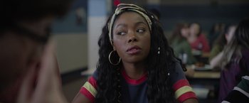 Movie still from “There's Someone Inside Your House” (2021), directed by Patrick Brice – A young woman with long black curly hair wearing a headband; Close Up shot, Over the shoulder angle