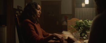 Movie still from “There's Someone Inside Your House” (2021), directed by Patrick Brice – A woman sitting at a table with papers in front of her; Medium shot, Over the shoulder angle