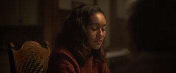 Movie still from “There's Someone Inside Your House” (2021), directed by Patrick Brice – A young girl sitting in the dark with her eyes closed; Close Up shot, Over the shoulder angle