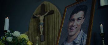 Movie still from “There's Someone Inside Your House” (2021), directed by Patrick Brice – A picture and crucifix in a room with flowers; Close Up shot, Low angle