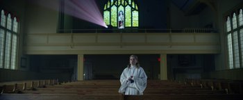 Movie still from “There's Someone Inside Your House” (2021), directed by Patrick Brice – A woman in a white robe standing in a church; Medium shot, Low angle