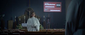 Movie still from “There's Someone Inside Your House” (2021), directed by Patrick Brice – A girl in a white robe stands in front of a church altar; Medium shot, Low angle