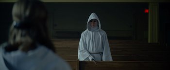 Movie still from “There's Someone Inside Your House” (2021), directed by Patrick Brice – A person in a white robe and a white hood; Medium shot, Over the shoulder angle