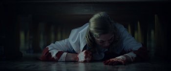 Movie still from “There's Someone Inside Your House” (2021), directed by Patrick Brice – A woman laying on the ground with blood on her hands; Medium shot, Low angle