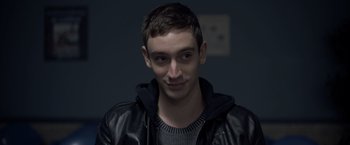 Movie still from “There's Someone Inside Your House” (2021), directed by Patrick Brice – A young man wearing a leather jacket and a sweater; Close Up shot, Low angle