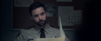 Movie still from “There's Someone Inside Your House” (2021), directed by Patrick Brice – A man in a uniform looking at a piece of paper in front of him; Close Up shot, Over the shoulder angle
