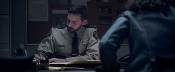 Movie still from “There's Someone Inside Your House” (2021), directed by Patrick Brice – A man sitting at a desk in front of papers; Medium shot, Over the shoulder angle
