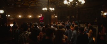 Movie still from “There's Someone Inside Your House” (2021), directed by Patrick Brice – A man in a red jacket is speaking to a crowd; Extreme Wide shot, Low angle