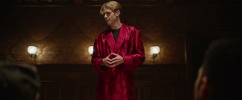 Movie still from “There's Someone Inside Your House” (2021), directed by Patrick Brice – A man in a red robe standing in front of a wall; Medium shot, Low angle