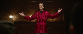 Movie still from “There's Someone Inside Your House” (2021), directed by Patrick Brice – A man in a red robe standing in front of a wall with his arms outstreched; Medium shot, Low angle