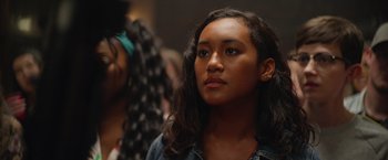 Movie still from “There's Someone Inside Your House” (2021), directed by Patrick Brice – A woman with long black hair is looking at the camera; Close Up shot, Over the shoulder angle