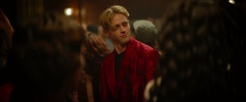 Movie still from “There's Someone Inside Your House” (2021), directed by Patrick Brice – A man in a red robe standing next to a crowd of onlookers; Close Up shot, Over the shoulder angle