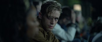 Movie still from “There's Someone Inside Your House” (2021), directed by Patrick Brice – A man with blonde hair sitting in front of a group of people; Close Up shot, Over the shoulder angle