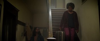 Movie still from “There's Someone Inside Your House” (2021), directed by Patrick Brice – A woman and a girl are standing on the stairs with suitcases; Medium shot, Low angle