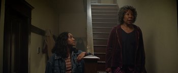 Movie still from “There's Someone Inside Your House” (2021), directed by Patrick Brice – Two women sitting on steps in front of a staircase; Medium shot, Low angle