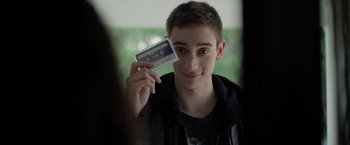 Movie still from “There's Someone Inside Your House” (2021), directed by Patrick Brice – A young man holding up an audio cassette; Close Up shot, Over the shoulder angle