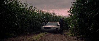 Movie still from “There's Someone Inside Your House” (2021), directed by Patrick Brice – Two people standing next to a car in a field; Extreme Wide shot, High angle