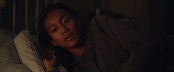 Movie still from “There's Someone Inside Your House” (2021), directed by Patrick Brice – A young woman sitting in a dark room with her head resting on her hand; Close Up shot, Over the shoulder angle