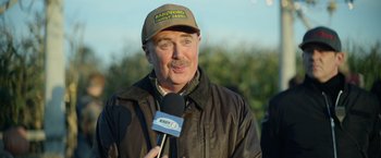 Movie still from “There's Someone Inside Your House” (2021), directed by Patrick Brice – A man in a brown jacket and a brown hat is holding a microphone; Close Up shot, Over the shoulder angle