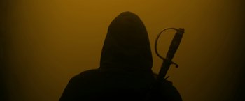Movie still from “There's Someone Inside Your House” (2021), directed by Patrick Brice – A person in a hooded sweatshirt holding a knife; Medium shot, Low angle