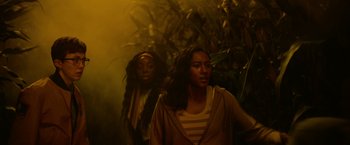 Movie still from “There's Someone Inside Your House” (2021), directed by Patrick Brice – Two women are walking through a forest with trees; Medium shot, Low angle