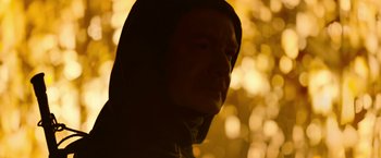 Movie still from “There's Someone Inside Your House” (2021), directed by Patrick Brice – A man in a hooded jacket is in front of some trees; Close Up shot, Low angle