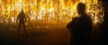 Movie still from “There's Someone Inside Your House” (2021), directed by Patrick Brice – A field of corn is burning in the dark; Extreme Wide shot, High angle