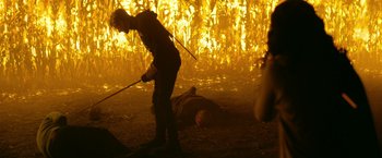 Movie still from “There's Someone Inside Your House” (2021), directed by Patrick Brice – A person is standing over a dead body in a corn field; Wide shot, Over the shoulder angle