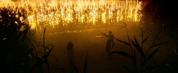 Movie still from “There's Someone Inside Your House” (2021), directed by Patrick Brice – Two people are standing in a field with a fire in the background; Extreme Wide shot, Low angle