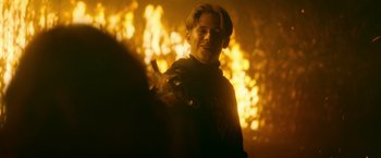 Movie still from “There's Someone Inside Your House” (2021), directed by Patrick Brice – A young man smiles in front of a fire background; Medium shot, Over the shoulder angle