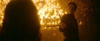 Movie still from “There's Someone Inside Your House” (2021), directed by Patrick Brice – A man holding a baseball bat while standing in front of a fire; Medium shot, Over the shoulder angle