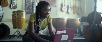 Movie still from “There's Someone Inside Your House” (2021), directed by Patrick Brice – A woman sitting in front of a laptop computer; Medium shot, Over the shoulder angle