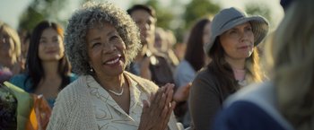 Movie still from “There's Someone Inside Your House” (2021), directed by Patrick Brice – An older woman claps her hands in front of a group of people; Close Up shot, Over the shoulder angle