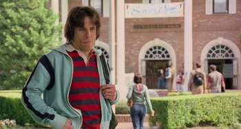 Movie still from “There's Something About Mary” (1998), directed by Bobby Farrelly – A young man walking down the sidewalk in front of a building; Medium shot, Over the shoulder angle