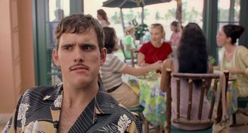 Movie still from “There's Something About Mary” (1998), directed by Bobby Farrelly – A young man with a mustache is sitting at a table with a group of people; Close Up shot, Over the shoulder angle