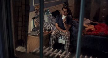 Movie still from “There's Something About Mary” (1998), directed by Bobby Farrelly – A man sitting on top of a bed holding a cup; Medium shot, High angle
