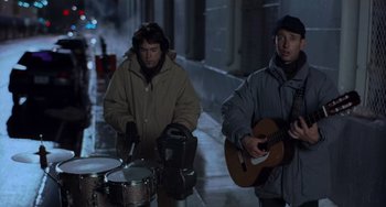 Movie still from “There's Something About Mary” (1998), directed by Bobby Farrelly – Two men on a street playing instruments while one of them plays a guitar; Medium shot, High angle